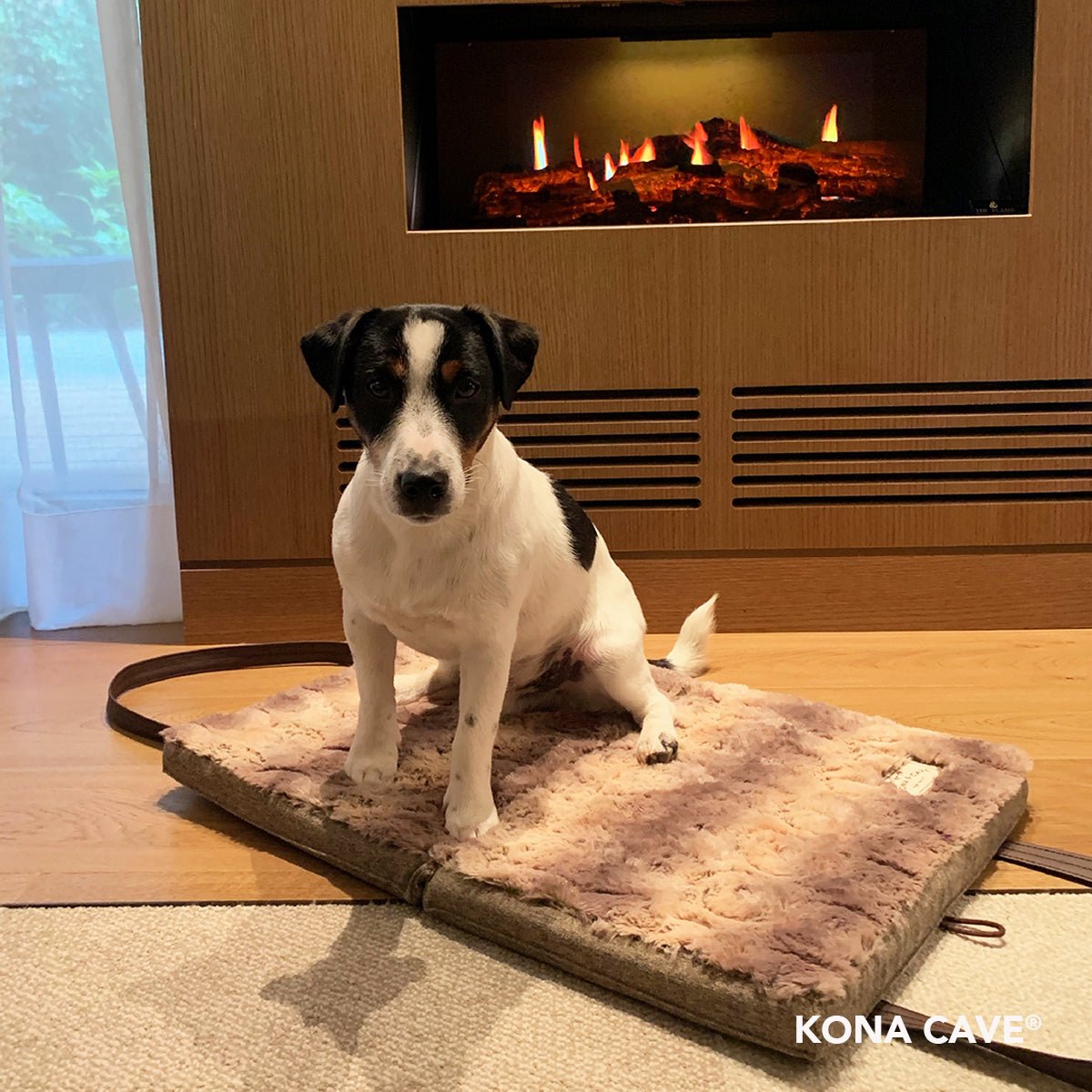 Adorable JRT in front of a fire on a KONA CAVE® folded, portable faux fur luxury travel dog bed great for hotel rooms. 