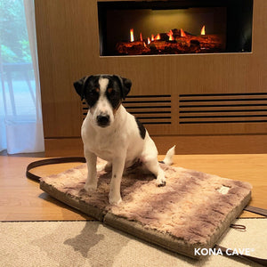 Adorable JRT in front of a fire on a KONA CAVE® folded, portable faux fur luxury travel dog bed great for hotel rooms. 